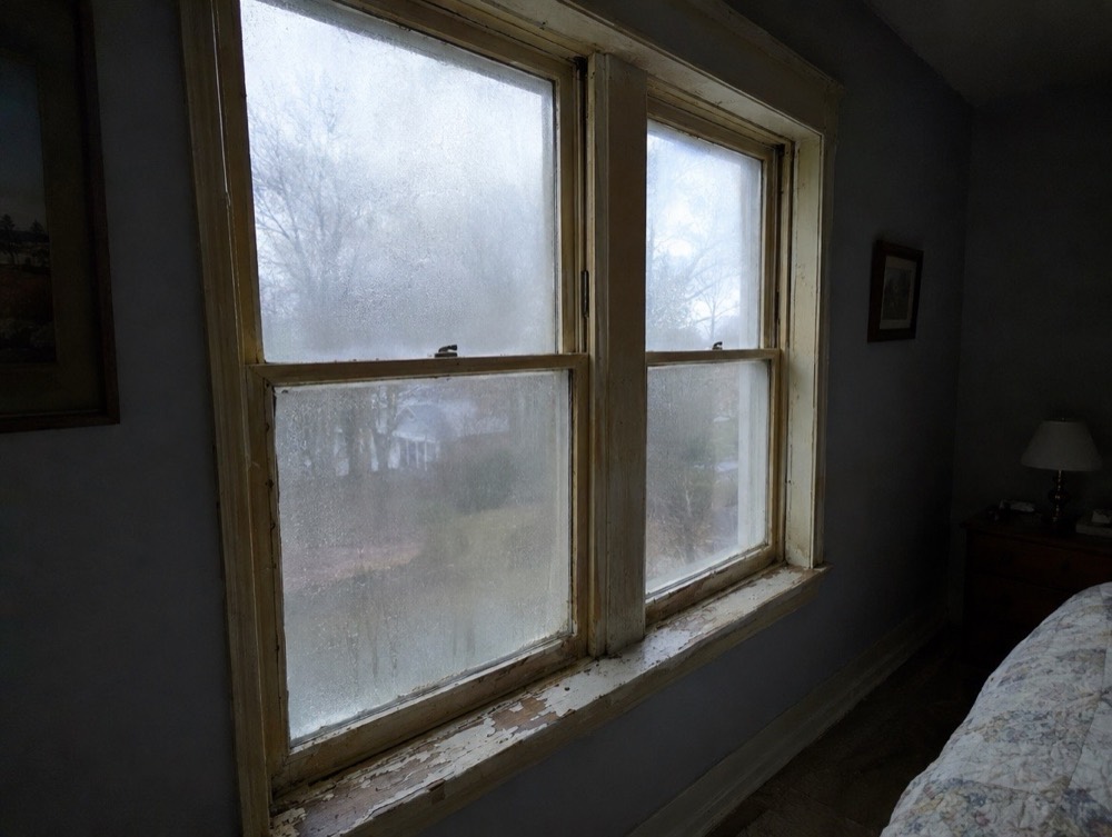 Drafty old bedroom windows with fogged glass and peeling wood frames